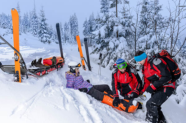 A skiier laying in snow being assisted by medical personnel